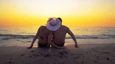 Romantik Çift balayına dokunmadan beach günbatımı ve Satım duyguları üzerinde oturuyor. Yaz dalgalar deniz onların legs splash.