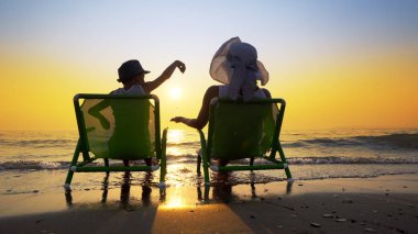 Aile dinlenmek günbatımı ve mavi gökyüzü arka plan ile tatil plaj sandalye üzerinde oturan kum ile oynamak