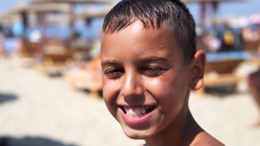 Handsome boy on beach look at camera and smile, the kid is dazzled by summer sun, cinematic dof clipart
