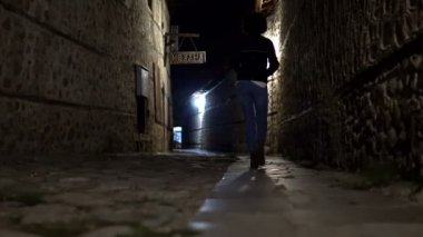 Geceleri taş döşeme ve duvar ile eski karanlık sokakta yürürken bir kadın silueti trekking. Eski ev ve sokak mimari Bansko, Bulgaristan