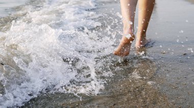 Çıplak ayaklı bir kadının deniz suyu dalgaları üzerinde yürümesi ve sıçraması, sinematik bir çekim.