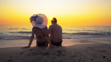 Romantik Çift balayına dokunmadan beach günbatımı ve Satım duyguları üzerinde oturuyor. Yaz dalgalar deniz onların legs splash.