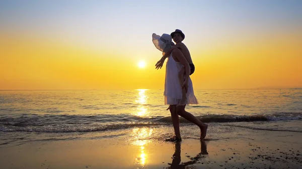 Mother gives her son a piggy back ride walking on empty ocean beach against sunset