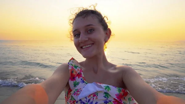 Beautiful teen in bikini makes funny selfie grimaces with summer sea sunset at background