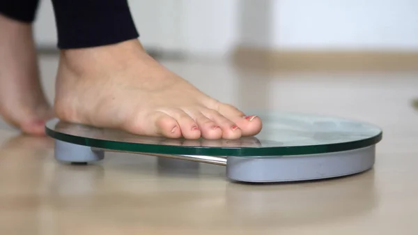 Girl feet on scales to measure the weight of the empty wooden floor