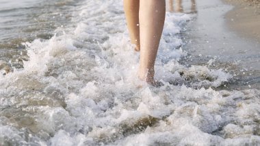 Çıplak ayaklı bir kadının deniz suyu dalgaları üzerinde yürümesi ve sıçraması, sinematik bir çekim.