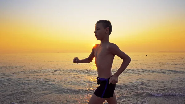 Sportjunge Läuft Strand Gegen Sonnenuntergang Hintergrund — Stockfoto