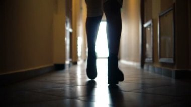 Ağır çekimde koridor boyunca koşan çizmeli kadın bacaklarının düşük kesimli silüeti ile sabit.