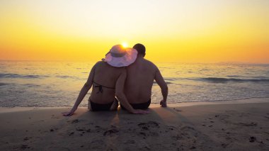 Romantik Çift balayına dokunmadan beach günbatımı ve Satım duyguları üzerinde oturuyor. Yaz dalgalar deniz onların legs splash.