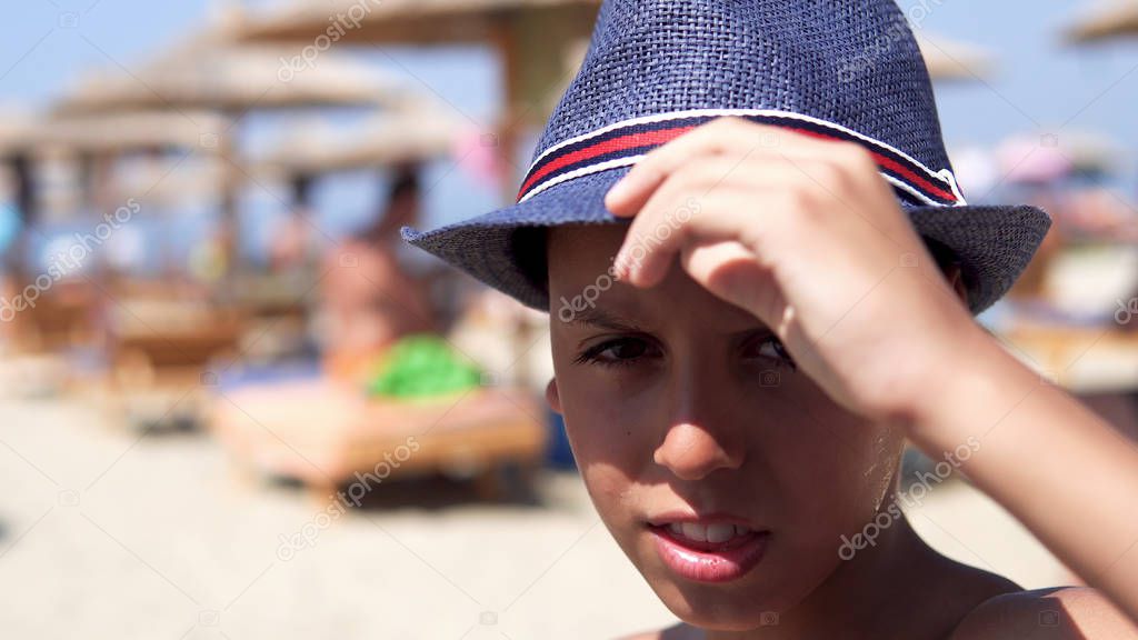Cute and handsome boy with hat poses at the beach smiling, selective focus