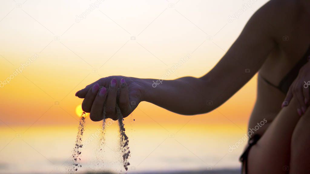 Happy female pours sand from the hand on sea beach sunset, concept of vacation, freedom, happiness, nature, travel