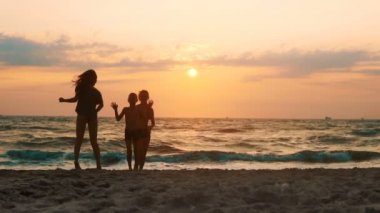 Group of happy children jump at the beach on sunset. Beauty and joyful teenager friends having fun, spraying over summer sunset, SLOW MOTION