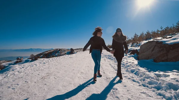 Two happy teen friends running on snow smiling, cinematic steadicam tracking shot