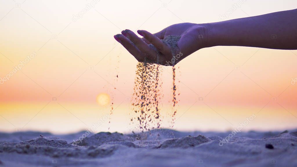 Woman with sand falling on the beach at sunset