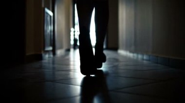 Ağır çekimde koridor boyunca koşan çizmeli kadın bacaklarının düşük kesimli silüeti ile sabit.