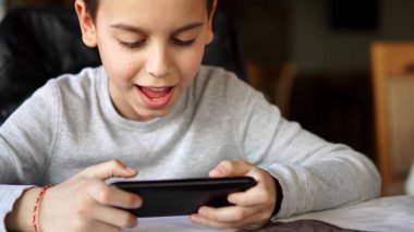 Masada oturan ve smartphone kullanarak gülümseyen mutlu çocuk