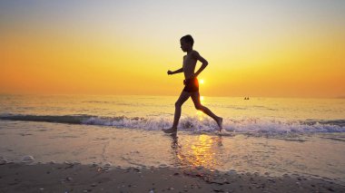 Arka plan gün batımında karşı deniz plaj üzerinde çalışan spor çocuk
