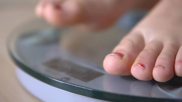 Female bare feet with weight scale on wooden floor, weight loss diet