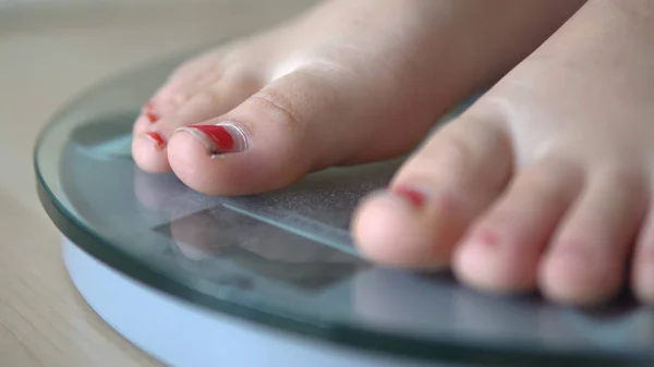 Girl feet on scales to measure the weight of the empty wooden floor