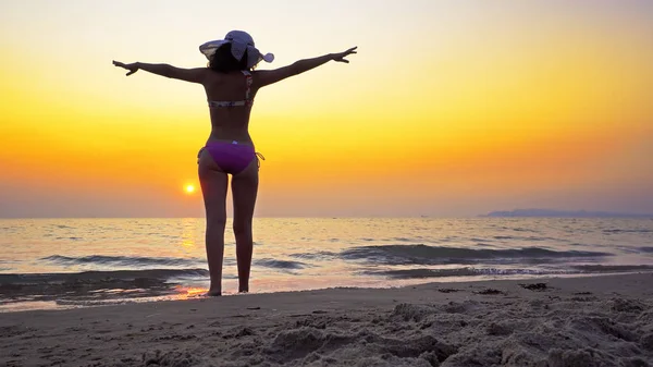Fit female teen with hat walk on an empty beach with wide open hands enjoying freedom. Girl enter sea water at sunset