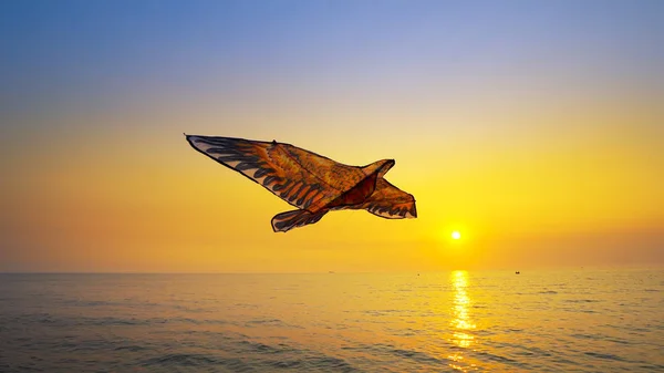 Close up colored toy kite flying high in air against gold sunset sky background sun on sea beach