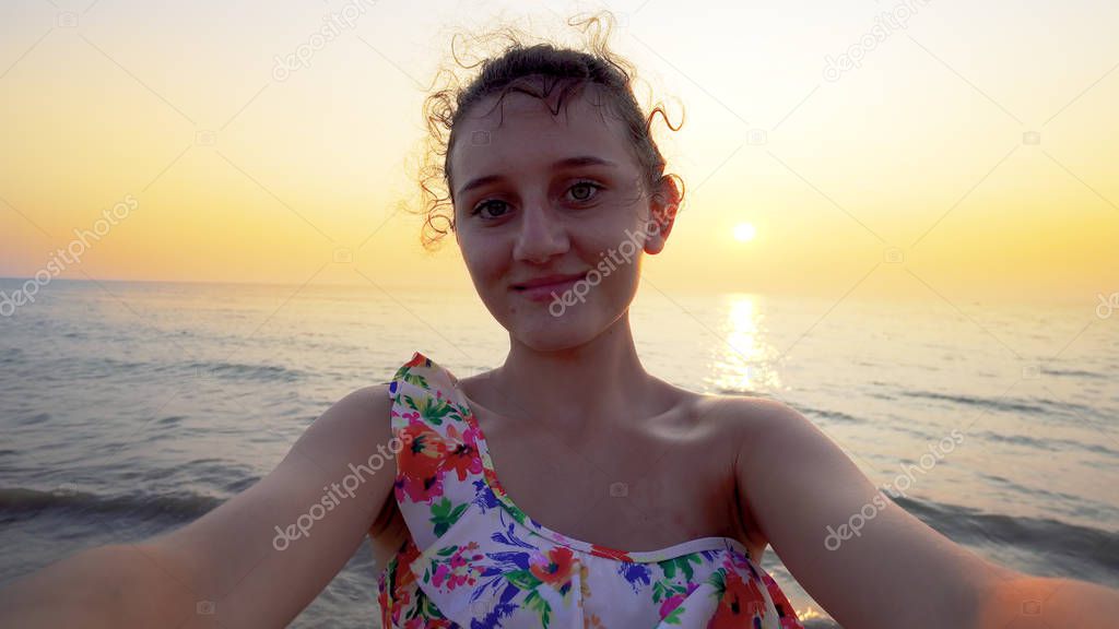Beautiful teen in bikini makes funny selfie grimaces with summer sea sunset at background