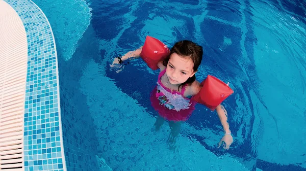 Girl with inflatable arm bands play in outdoor pool