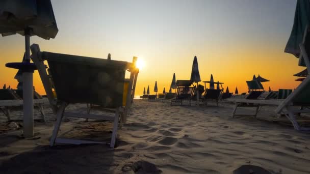夕日に対するサンシェードとサンベッド付きのビーチ 旅行のコンセプトの背景 — ストック動画