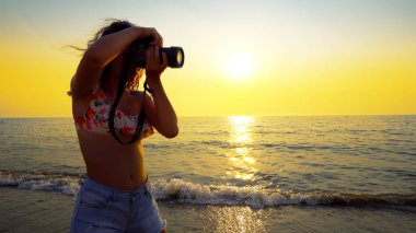 Plaj günbatımının fotoğrafını çeken bir turist. Fotoğrafçı kız DSLR aynasız kamera kullanarak fotoğraf çekiyor.