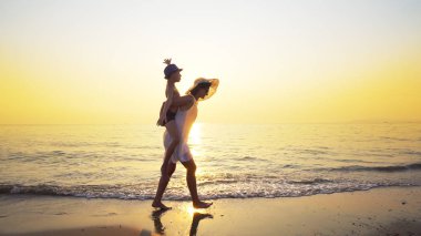 Sevgi dolu aile sahilde eğleniyor. Çocuk anneler geri ayaklarının Okyanusu günbatımı karşı sıçramasına dalgalar ile sürme domuz binmek. Steadicam atış