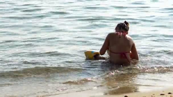 独自的女孩坐在浅海水的沙滩上 — 图库视频影像
