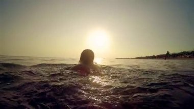 Woman playing swimming in the sea at sunset, trekking shot