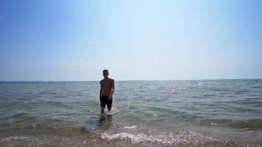Yakışıklı sporcu erkek, deniz sahilinde sudan çıkıyor. Sinema filmi gibi.