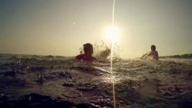 Okyanusta oynama ve sıçramasına mutlu aile siluetleri günbatımında - Slow Motion tropik bir adada tatil turist su