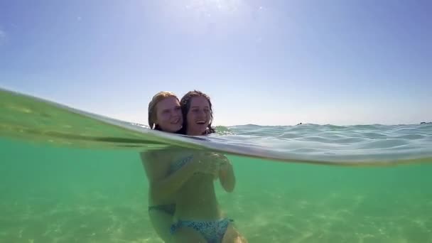 两个不同民族的少女的美丽肖像拥抱和亲吻 微笑着在一个宽敞的绿松石海在一个暑假 旅行生活方式 自然海滩外观 戈普罗圆顶半水下景观 慢动作 — 图库视频影像
