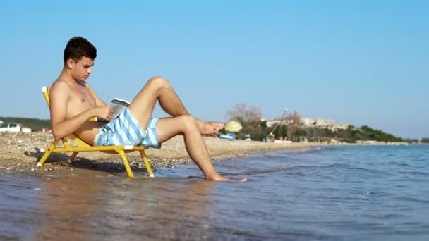 Mannen Stoel Lezing Boek Het Strand Filmische Dof — Stockvideo