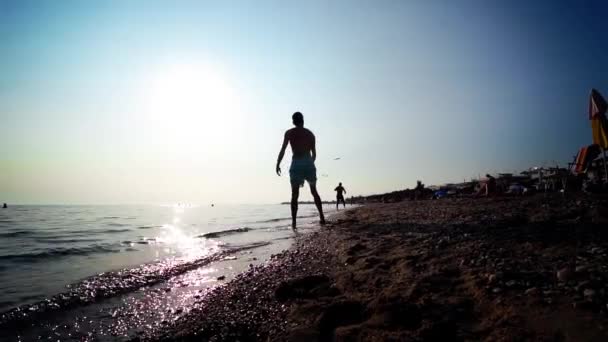 在夏日阳光照射下的海滩上玩飞盘的剪影人 — 图库视频影像