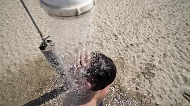 Jeune homme laver les cheveux sous la douche de plage 