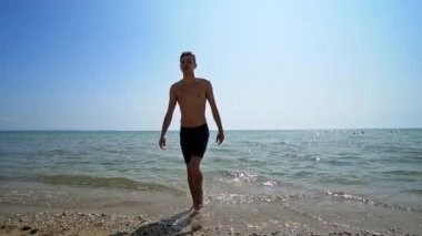 Handsome athlete male walk out of water on sea beach, cinematic steadicam shot, SLOW MOTION