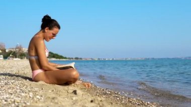 Genç kadınlar sahilde kitap okuyarak tatilden zevk alıyorlar.