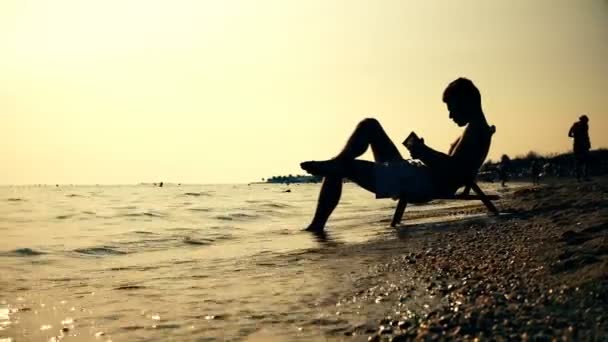 Silhouette Uomini Sedia Lettura Libro Sulla Spiaggia Tramonto Alba Dof — Video Stock