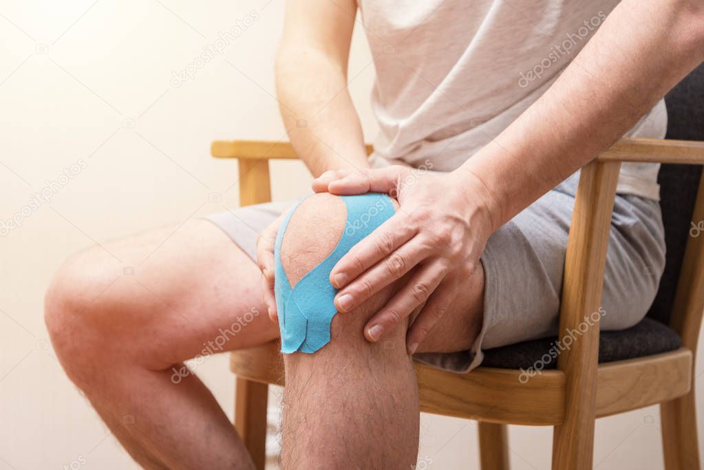 Man sitting on the chair and holding his sore knee with Kinesiol