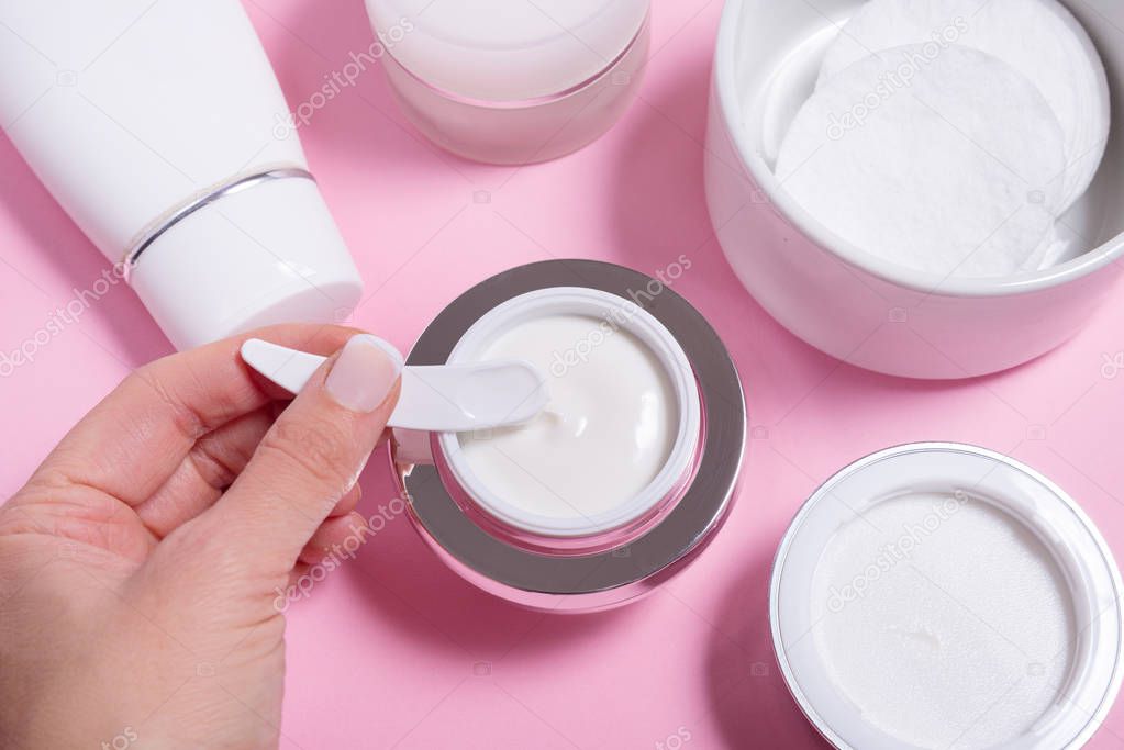 Set of face cream bottles on pink background, hand holding cosme