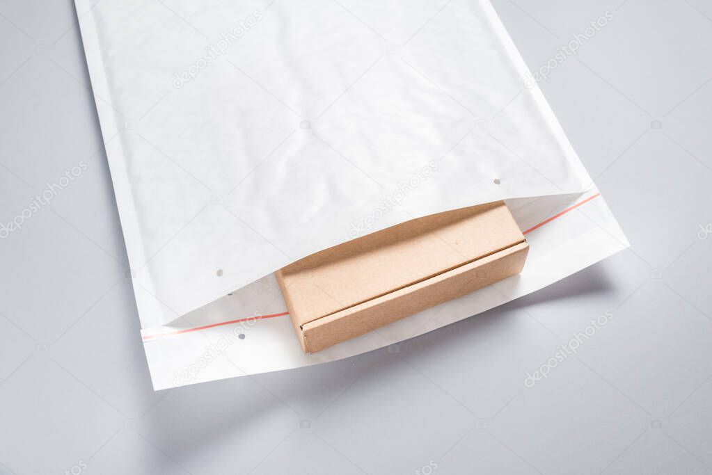 Brown cardboard box packed in white bubble envelopes on grey bac