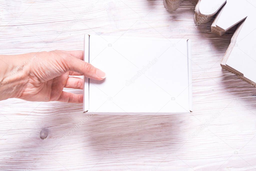 Woman hand holding square carton boxes on wooden background, cut