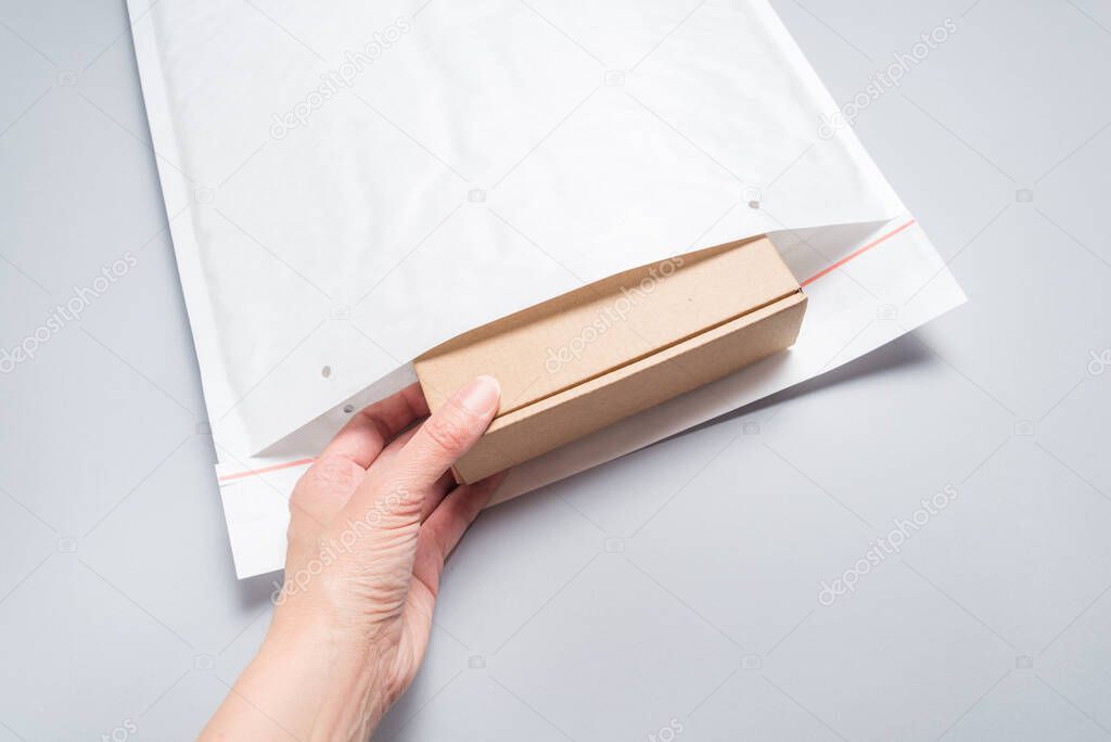 Hand put brown cardboard box to white bubble envelopes on grey b