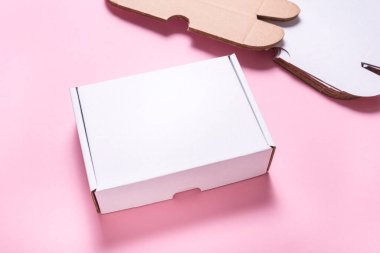 Beyaz karton düz posta kutusu, çanta, pembe masanın üstünde.