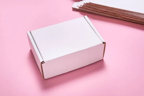 White cardboard flat postal box, case, on pink desk