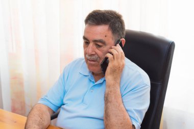 Neşeli kıdemli telefonda konuşurken dizüstü bilgisayarda çalışan adam