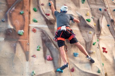 Young man practicing rock climbing on artificial wall indoors. clipart